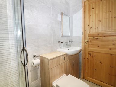 A bathroom with a shower cubicle a wooden door a sink with a cabinet and a toilet at Kipling Lodge in Rudyard