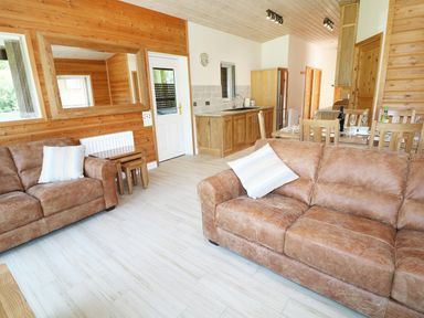 A living area with two brown sofas a wooden dining table and an open kitchen at Kipling Lodge in Rudyard