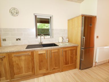 A kitchen with wooden cabinets a sink a stainless steel refrigerator and a wall clock at Kipling Lodge in Rudyard