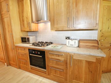 A kitchen with wooden cabinets a gas stove an oven a microwave a toaster and a wooden bread box at Kipling Lodge in Rudyard