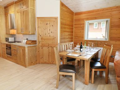 A kitchen and dining area with wooden cabinets a dining table with chairs and a window at Kipling Lodge in Rudyard