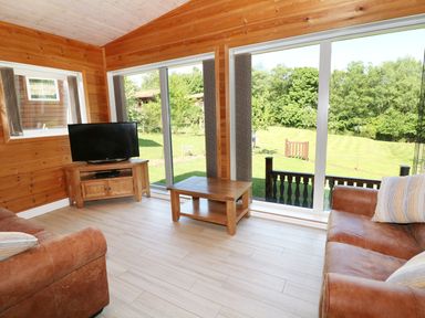 A living room with large windows brown leather sofas wooden table and television at Kipling Lodge in Rudyard