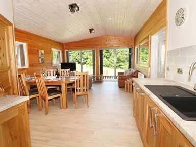 A kitchen and dining area with wooden furniture and sliding glass doors overlooking greenery at Kipling Lodge in Rudyard