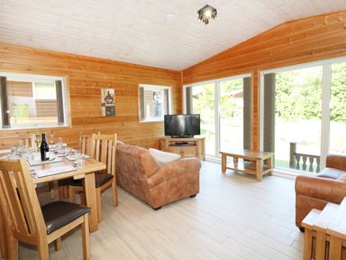 A wooden interior living room with two brown sofas a dining table with chairs a TV on a wooden stand and large windows at Kipling Lodge in Rudyard