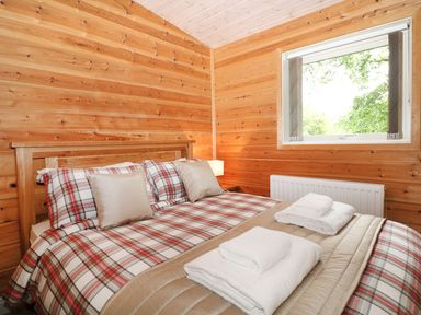 A wooden bedroom with a double bed covered in plaid bedding and two folded towels at Kipling Lodge in Rudyard