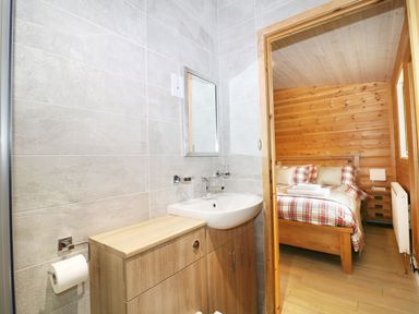 A bathroom with a sink and wooden cabinet next to a bedroom with a bed and wooden walls at Kipling Lodge in Rudyard
