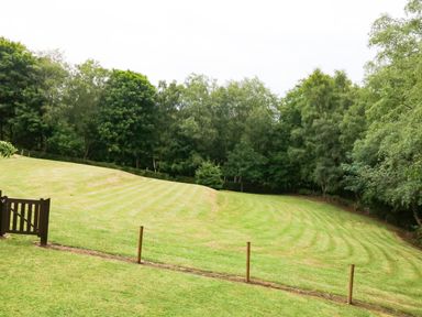 A grassy yard with a wooden gate and fence posts bordered by trees at Kipling Lodge in Rudyard