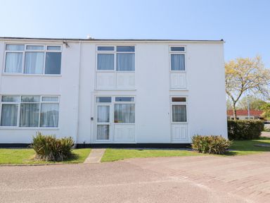 A white two-story building with multiple windows and doors surrounded by grass and plants at La Capsule in Dawlish Warren