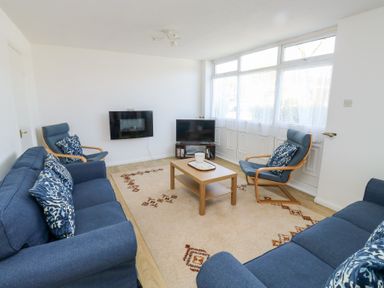 A living room with blue sofas and armchairs around a wooden coffee table near a television at La Capsule in Dawlish Warren