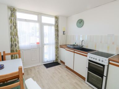 A kitchen with a stove sink wooden countertop and dining table near a window with curtains at La Capsule in Dawlish Warren