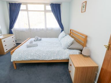 A bedroom with a double bed and blue curtains beside large windows at La Capsule in Dawlish Warren