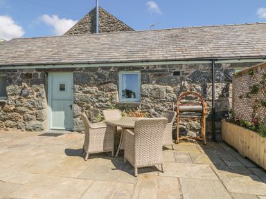 An outdoor patio area with a stone house wall and a round table surrounded by four wicker chairs at Cornel Glyd in Talybont near Barmouth