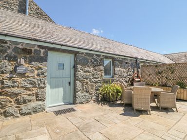 An outdoor patio with stone walls a light blue door and a table with four wicker chairs at Cornel Glyd in Talybont near Barmouth