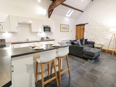 A kitchen and living area with a black countertop and white stools next to a gray sofa with cushions at Cornel Glyd in Talybont near Barmouth