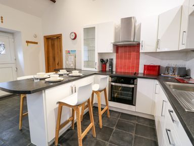A kitchen with white cabinets black countertops a red tile backsplash and two stools at Cornel Glyd in Talybont near Barmouth