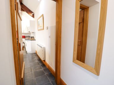 A narrow hallway with a wall-mounted radiator and a mirror leading to a kitchen at Cornel Glyd in Talybont near Barmouth