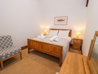 A bedroom with a wooden bed frame bedside tables with lamps a patterned chair and a wooden dresser with mirror at Cornel Glyd in Talybont near Barmouth