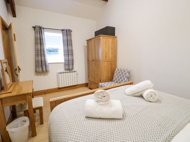 A bedroom with a bed with towels a wooden wardrobe a chair and a wooden dressing table at Cornel Glyd Talybont near Barmouth