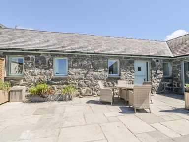 An outdoor patio area with stone flooring stone walls a table with four wicker chairs and potted plants at Sisial-y-Mor in Talybont near Barmouth
