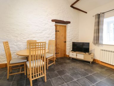 A dining area with a wooden table and four chairs a wooden door a television on a stand and a window with plaid curtains at Sisial-y-Mor in Talybont near Barmouth