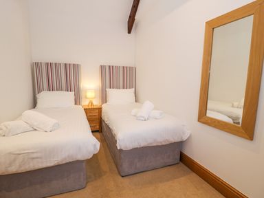 A bedroom with two single beds a wooden nightstand with a lamp and a wall mirror at Sisial-y-Mor in Talybont near Barmouth