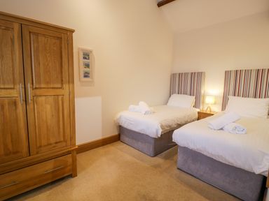 A bedroom with two single beds with striped headboards and a wooden wardrobe at Sisial-y-Mor in Talybont near Barmouth