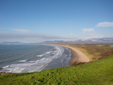 A coastal landscape with a sandy beach and grassy hills at Sisial-y-Mor in Talybont near Barmouth