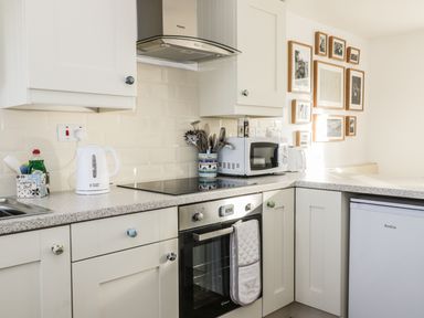A kitchen with white cabinets a microwave oven kettle and a collection of framed pictures on the wall at 1 Dunkirk Cottages Humshaugh near Hexham