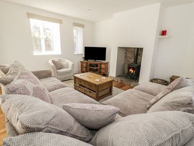A living room with a large sectional sofa a white armchair a wooden coffee table a television on a wooden stand and a fireplace at 1 Dunkirk Cottages in Humshaugh near Hexham