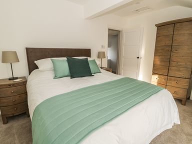 A bedroom with a bed green bedspread pillows wooden bedside tables lamps and a wooden wardrobe at 1 Dunkirk Cottages in Humshaugh near Hexham