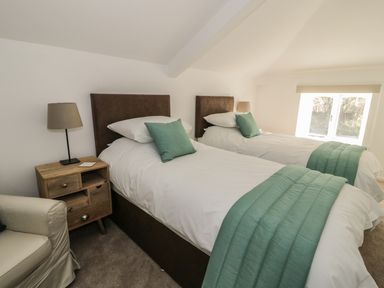 A bedroom with two single beds with green pillows and throws and a wooden nightstand with a lamp at 1 Dunkirk Cottages in Humshaugh near Hexham
