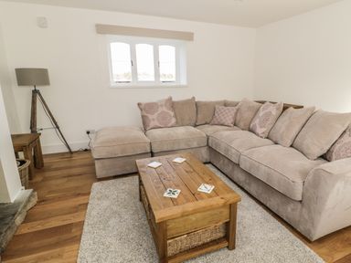 A living room with a large beige sectional sofa cushions wooden coffee table and tripod floor lamp at 1 Dunkirk Cottages in Humshaugh near Hexham