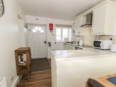 A kitchen with white cabinets appliances and a wooden wine rack near the door at 1 Dunkirk Cottages Humshaugh near Hexham