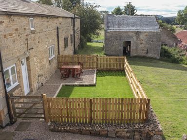 A fenced garden with grass and a wooden table set next to a stone building at 1 Dunkirk Cottages in Humshaugh near Hexham