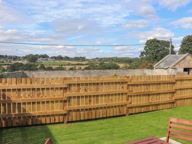 A backyard with a wooden fence a stone wall and a small stone shed with a slate roof in the countryside at 1 Dunkirk Cottages in Humshaugh near Hexham