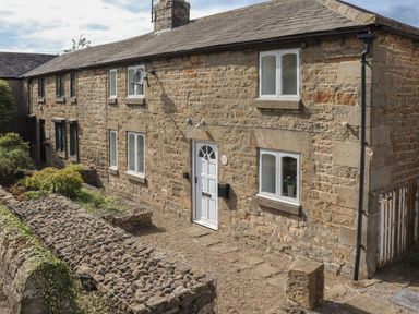 Exterior view of a stone cottage with white door and windows and a gravel pathway at 1 Dunkirk Cottages Humshaugh near Hexham