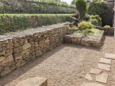 A garden area with wire-encased stone walls gravel ground and planted shrubs at 1 Dunkirk Cottages in Humshaugh near Hexham