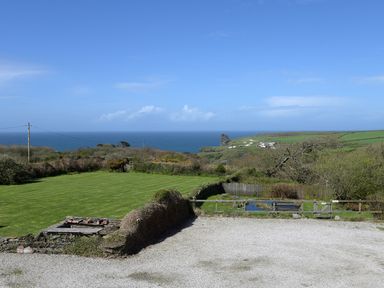 A landscape view of a grassy yard with a gravel area and wooden fence overlooking the ocean and hills at Threshings Cottage in Tintagel