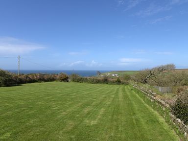 A grassy field with stone walls and bushes overlooking the sea at Threshings Cottage in Tintagel