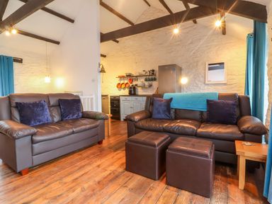 A living room with two leather sofas and ottomans near a kitchen area at Threshings Cottage in Tintagel