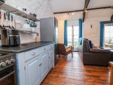 A kitchen with blue cabinets and black countertop next to a living area with leather sofa and armchair at Threshings Cottage in Tintagel