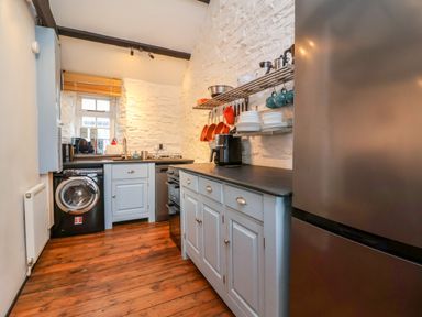 A kitchen with wooden floor white cabinets black appliances and shelves with dishes at Threshings Cottage in Tintagel