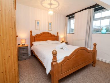 A bedroom with a wooden double bed white bedding bedside tables lamps wardrobe and two windows at Threshings Cottage in Tintagel