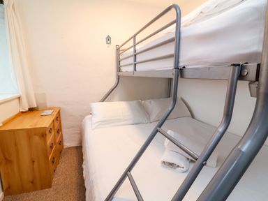 A bedroom with a metal bunk bed bed side table and window with curtains at Threshings Cottage in Tintagel