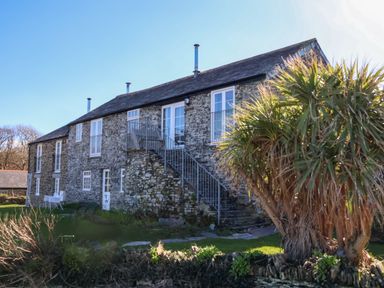 Stone building with external metal staircase and palm tree in front at Threshings Cottage in Tintagel