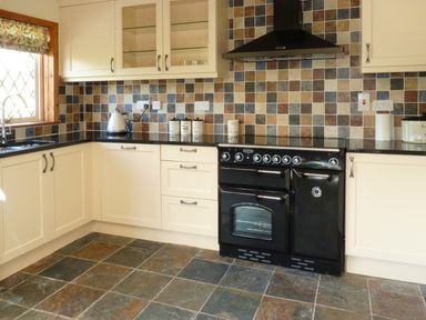 A kitchen with a black oven cooker cream cabinets black countertops tiled backsplash and tiled floor at Fig Tree Cottage in Bickleigh