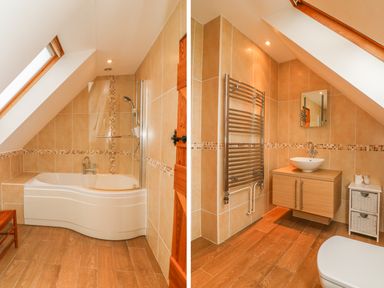 A bathroom with a bathtub and shower under a sloped ceiling and a sink with mirror and towel rack at Fig Tree Cottage in Bickleigh