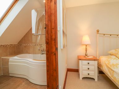 A bathroom with a bathtub and a bedroom with a bedside table lamp and bed at Fig Tree Cottage in Bickleigh