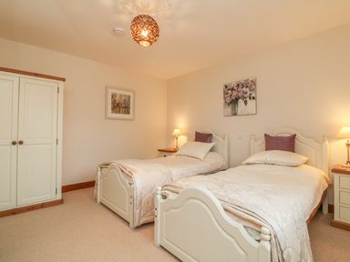 A bedroom with two single beds two bedside tables with lamps a wardrobe and two paintings at Fig Tree Cottage in Bickleigh