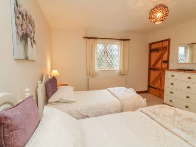 A bedroom with two single beds a wooden door a window with curtains and a dresser at Fig Tree Cottage in Bickleigh